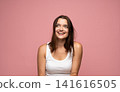 Young woman smiling, looking up and thinking, experiencing positive emotions against a pink background 141616505