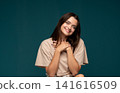 Young woman showing gratitude and appreciation, smiling with hands on chest against a dark background 141616509