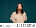 Young woman making a kissy face against a deep teal background, expressing playful love and affection 141616510