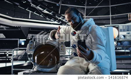 Astronaut records selfie video with smartphone, making hand gestures, speaking to subscribers during Mars mission. Cosmonaut recording cosmic exploration content for followers Astronaut records selfie video with smartphone, making hand gestures, speaking to subscribers during Mars mission. Cosmonaut recording cosmic exploration content for followers 141616874