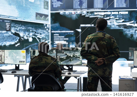 Army supervisor monitors geospatial surveillance feed on screens in military operations room. Intelligence agency team analyzing satellite maps to gather defensive operation intel Army supervisor monitors geospatial surveillance feed on screens in military operations room. Intelligence agency team analyzing satellite maps to gather defensive operation intel 141616927
