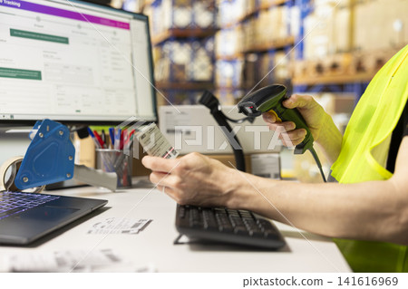 Asian worker scanning and printing shipping labels tags for all orders, using a scanner to register and check stock barcodes for fast delivery operations. Warehouse cargo placed on big racks. Asian worker scanning and printing shipping labels tags for all orders, using a scanner to register and check stock barcodes for fast delivery operations. Warehouse cargo placed on big racks. 141616969