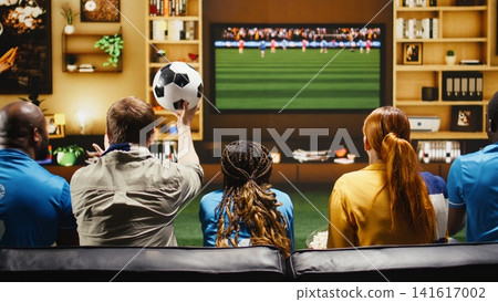Close up of football supporters eating popcorn and drinking beer while watching live match on TV. Group of friends holding fan props enjoying snacks during home watch party, having fun Close up of football supporters eating popcorn and drinking beer while watching live match on TV. Group of friends holding fan props enjoying snacks during home watch party, having fun 141617002