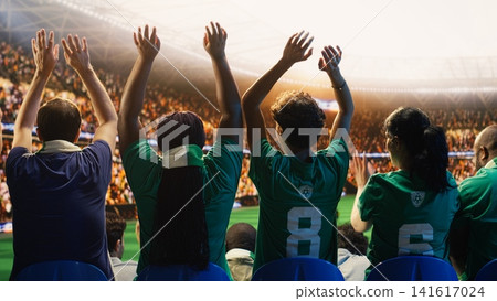 Rear view of football supporters starting crowd wave across packed stadium rows during match. Back view of soccer fans doing choreography to create electrifying stadium energy motivating players Rear view of football supporters starting crowd wave across packed stadium rows during match. Back view of soccer fans doing choreography to create electrifying stadium energy motivating players 141617024