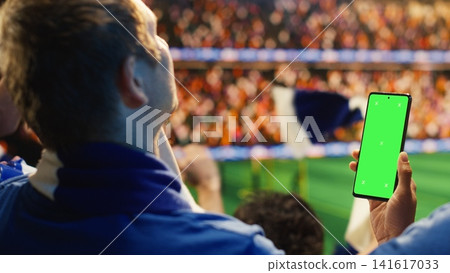 Chroma key smartphone used by football supporter in stadium to follow live scores. Soccer fan checks betting app on green screen phone during match day Chroma key smartphone used by football supporter in stadium to follow live scores. Soccer fan checks betting app on green screen phone during match day 141617033