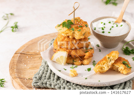 Crispy golden cod fish fritters stacked on a rustic plate with creamy dipping sauce fresh herbs and a lemon wedge for a perfect appetizer snack Crispy golden cod fish fritters stacked on a rustic plate with creamy dipping sauce fresh herbs and a lemon wedge for a perfect appetizer snack 141617627