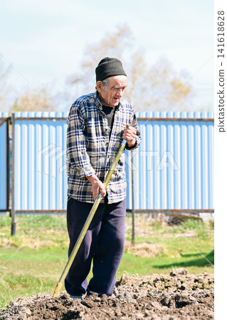 Tired russian 77 years old elderly man leans on shovel taking break from digging soil in rural village vegetable garden Tired russian 77 years old elderly man leans on shovel taking break from digging soil in rural village vegetable garden 141618628