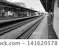 A monochrome photograph of the quiet platform and stretching tracks at Higashi-Fushimi Station on the Seibu Shinjuku Line in Tokyo. 141620578