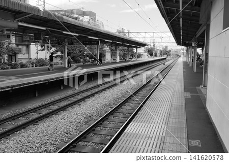 A monochrome photograph of the quiet platform and stretching tracks at Higashi-Fushimi Station on the Seibu Shinjuku Line in Tokyo. A monochrome photograph of the quiet platform and stretching tracks at Higashi-Fushimi Station on the Seibu Shinjuku Line in Tokyo. 141620578