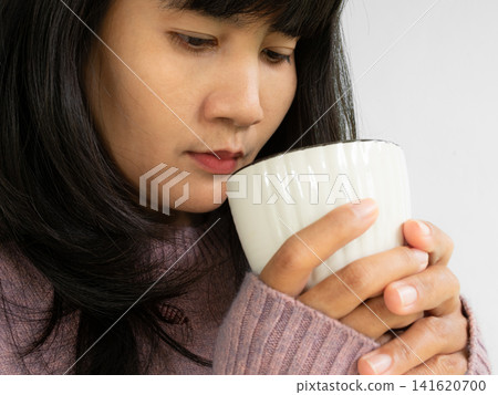 Autumn drink, woman with sweater holding hot chocolate cup at home in mornig, portrait lifestyle relax break enjoy carefree on winter season, asian skin tan and brown hair. Autumn drink, woman with sweater holding hot chocolate cup at home in mornig, portrait lifestyle relax break enjoy carefree on winter season, asian skin tan and brown hair. 141620700