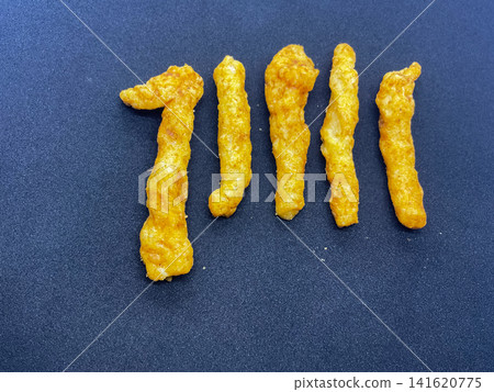 Spicy Indian Kurkure Corn Puff Snacks namkeen sticks arranged neatly in a row on a clean black backdrop. Spicy Indian Kurkure Corn Puff Snacks namkeen sticks arranged neatly in a row on a clean black backdrop. 141620775