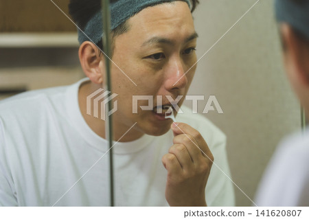A man in his 40s using dental floss in front of the bathroom mirror. A man in his 40s using dental floss in front of the bathroom mirror. 141620807