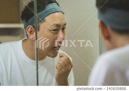 A man in his 40s using dental floss in front of the bathroom mirror. A man in his 40s using dental floss in front of the bathroom mirror. 141620808