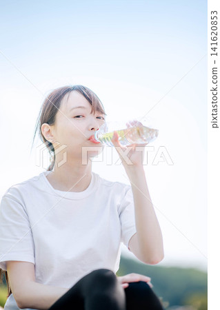 一名女子在戶外喝瓶裝水補充水分。 一名女子在戶外喝瓶裝水補充水分。 141620853