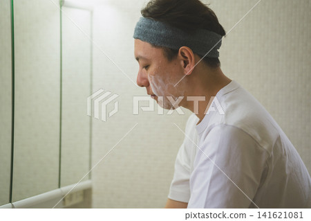 一位四十多歲的男子在浴室裡使用泡沫潔面乳的側面照。 一位四十多歲的男子在浴室裡使用泡沫潔面乳的側面照。 141621081