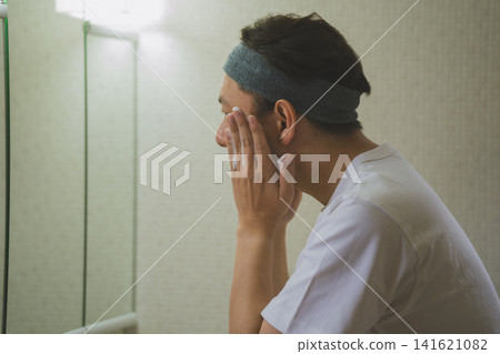 一位四十多歲的男子在浴室鏡子前進行護膚的側面照。 141621082