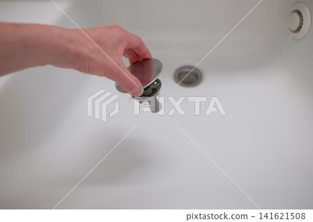 一隻女人的手正在清理浴室水槽的排水管。 一隻女人的手正在清理浴室水槽的排水管。 141621508