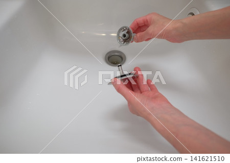 一隻女人的手正在清理浴室水槽的排水管。 一隻女人的手正在清理浴室水槽的排水管。 141621510