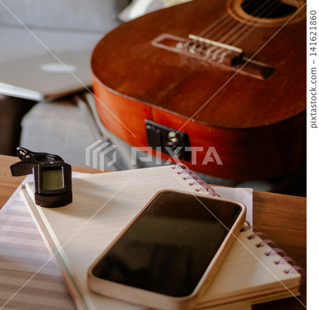 Musician working on songwriting and composing new music, using an acoustic guitar, notebook, smartphone, and tuner for creative artistic expression Musician working on songwriting and composing new music, using an acoustic guitar, notebook, smartphone, and tuner for creative artistic expression 141621860