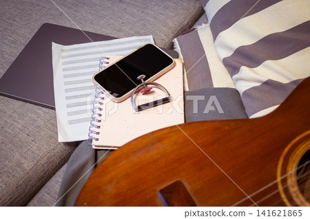 Acoustic guitar, sheet music, a smartphone, notebook, and capo arranged on a cozy couch, representing the process of songwriting, creative work, and home practice Acoustic guitar, sheet music, a smartphone, notebook, and capo arranged on a cozy couch, representing the process of songwriting, creative work, and home practice 141621865