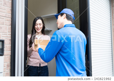 A young woman receiving a package from a delivery person: A lifestyle image. A young woman receiving a package from a delivery person: A lifestyle image. 141621992