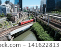 A dynamic view of a Marunouchi Line train crossing the Kanda River in Ochanomizu, Tokyo, with a green railway bridge in the background. 141622813