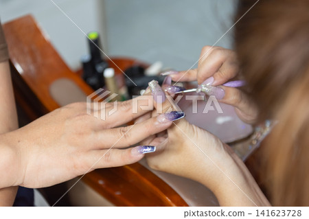 Closeup of nail technician applying gel polish during professional manicure elegant purple glitter acrylic nails beauty salon focused nail care style Closeup of nail technician applying gel polish during professional manicure elegant purple glitter acrylic nails beauty salon focused nail care style 141623728