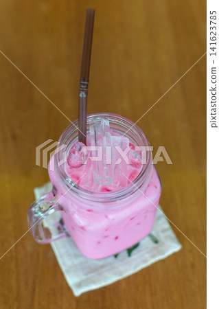 Refreshing pink iced milk drink served glass mug ice cubes straw wooden table perfect for cafe menu dessert beverage summer refreshment Refreshing pink iced milk drink served glass mug ice cubes straw wooden table perfect for cafe menu dessert beverage summer refreshment 141623785