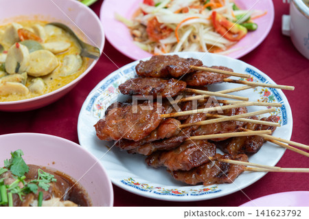 Thai grilled pork skewers served papaya salad curry dining table Traditional street food meal rich flavors perfect for lunch dinner local cuisine Thai grilled pork skewers served papaya salad curry dining table Traditional street food meal rich flavors perfect for lunch dinner local cuisine 141623792