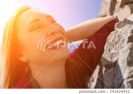 Woman smiling sunlight joyful adult woman leaning against a stone wall enjoying the warmth of a bright sunny day outdoors Woman smiling sunlight joyful adult woman leaning against a stone wall enjoying the warmth of a bright sunny day outdoors 141624452