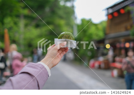 A close-up of a woman eating a steamed bun while walking around a retro tourist spot in Tokyo (a public road near Jindaiji Temple). 141624924