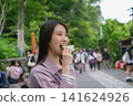 一位女士在東京一處復古旅遊景點（深大寺附近的一條公共道路）吃街頭小吃。 141624926