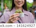一位女士在東京一處復古旅遊景點（深大寺附近的一條公共道路）邊走邊吃包子的特寫鏡頭。 141624927