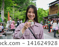 一位女士在東京一處復古旅遊景點（深大寺附近的一條公共道路）邊走邊吃包子的特寫鏡頭。 141624928