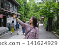 一位微笑的女士在東京一處復古旅遊景點（深大寺附近的一條公共道路）用智慧型手機拍照。 141624929
