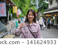 一張東京復古旅遊景點（深大寺附近的一條公共道路）上，一位微笑的女子正在吃街頭小吃的肖像。 141624933