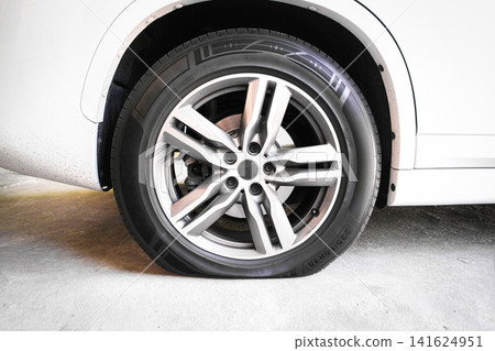 Close-up of a flat tire on a white modern car parked on a concrete floor Close-up of a flat tire on a white modern car parked on a concrete floor 141624951