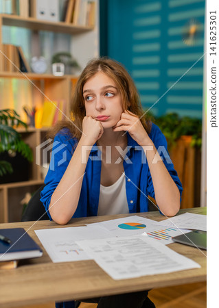 Young woman on home table feeling tired and upset after failed work day leaning on hand indoors sad Young woman on home table feeling tired and upset after failed work day leaning on hand indoors sad 141625301