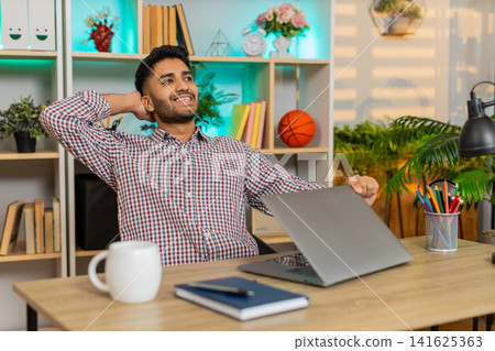 Indian man on home table closing laptop with satisfied smile after productive work routine indoors Indian man on home table closing laptop with satisfied smile after productive work routine indoors 141625363