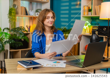 Young woman on home table checking documents finds needed point and nods with satisfied happy smile Young woman on home table checking documents finds needed point and nods with satisfied happy smile 141625543