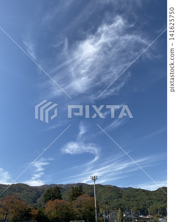 A landscape of delicate cirrus clouds spreading across a blue sky and mountains adorned with autumn foliage. A landscape of delicate cirrus clouds spreading across a blue sky and mountains adorned with autumn foliage. 141625750