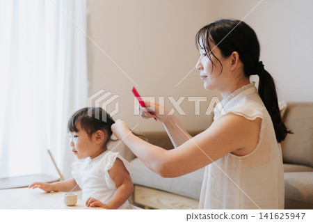 Mother tying her daughter's hair / child's hair styling Mother tying her daughter's hair / child's hair styling 141625947