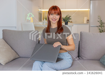 Young woman closes laptop looks at camera gentle smile work shift complete end of workday satisfied 141626041