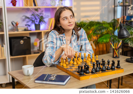 Young woman on home table playing chess board game with thoughtful strategy in living room indoors Young woman on home table playing chess board game with thoughtful strategy in living room indoors 141626066