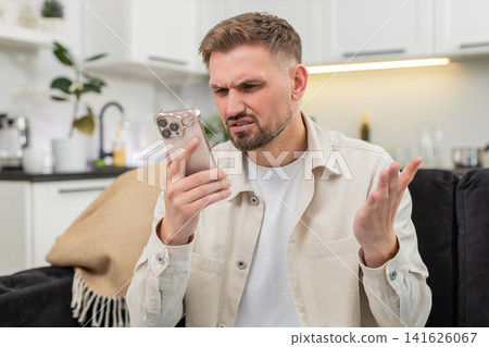 Young man gets alarming smartphone alert frowns asks why it happened anxious reaction worried mood Young man gets alarming smartphone alert frowns asks why it happened anxious reaction worried mood 141626067