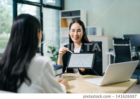 Professional Asian real estate consultant presenting a house model to a client during a property investment meeting in a modern office. Professional Asian real estate consultant presenting a house model to a client during a property investment meeting in a modern office. 141626087