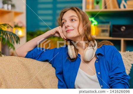 Young woman on home sofa enjoying calm pause and looking aside with peaceful smile indoors at home Young woman on home sofa enjoying calm pause and looking aside with peaceful smile indoors at home 141626096