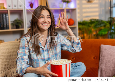Young woman on home sofa eating popcorn while watching tv and laughing with cheerful playful mood Young woman on home sofa eating popcorn while watching tv and laughing with cheerful playful mood 141626128