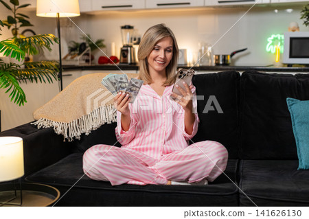 Woman counts money cash dollars with smartphone plans budget notes check salary income saving record Woman counts money cash dollars with smartphone plans budget notes check salary income saving record 141626130
