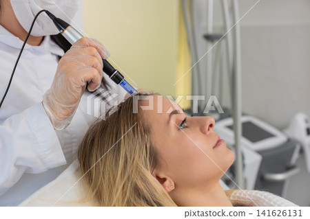 Woman receives microneedling and injections for hair growth scalp therapy in trichology clinic Woman receives microneedling and injections for hair growth scalp therapy in trichology clinic 141626131